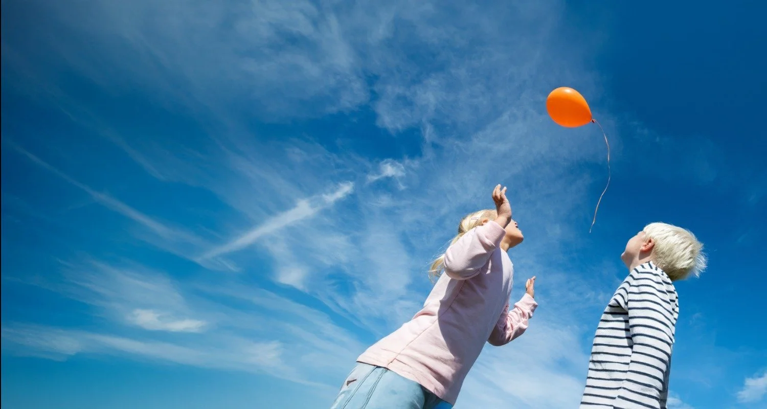 Dos niños jugando con un globo bajo un cielo azul
